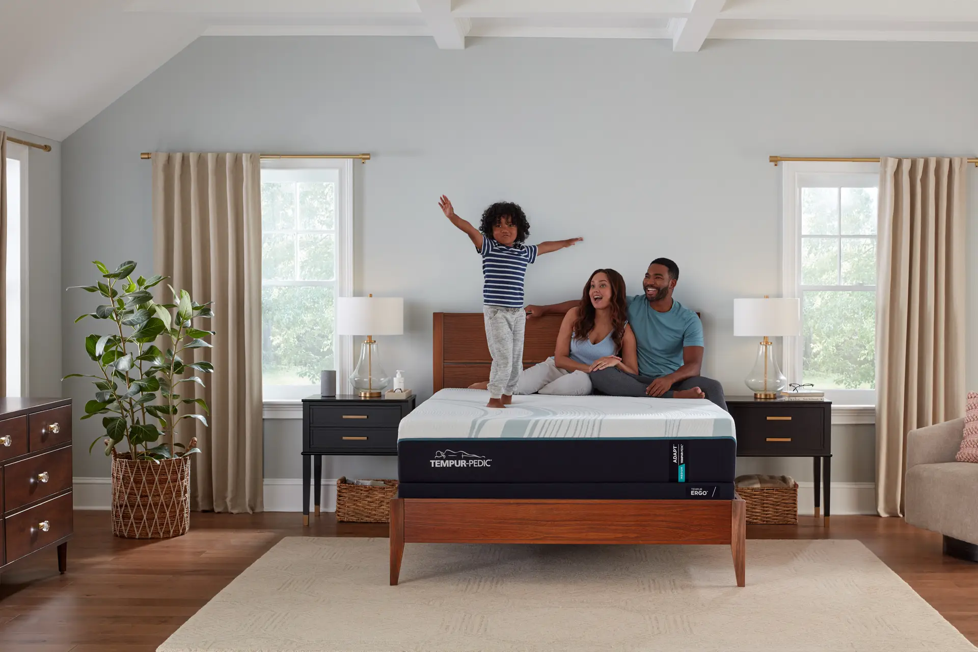 Family enjoying a TEMPUR-Adapt® mattress in a cozy bedroom, with a child playfully standing on the bed, highlighting comfort and relaxation.