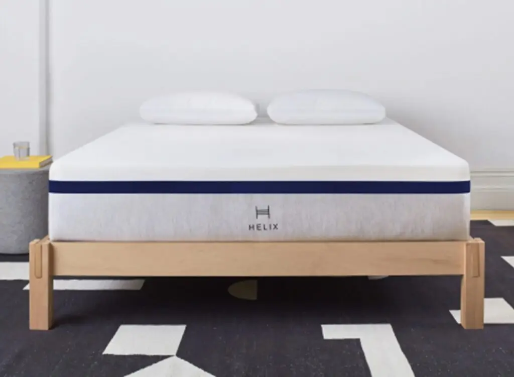 Helix mattress displayed on a wooden bed frame with two pillows, showcasing modern design and comfort, relevant to Jacksonville Bedding's Grand Opening promotions.