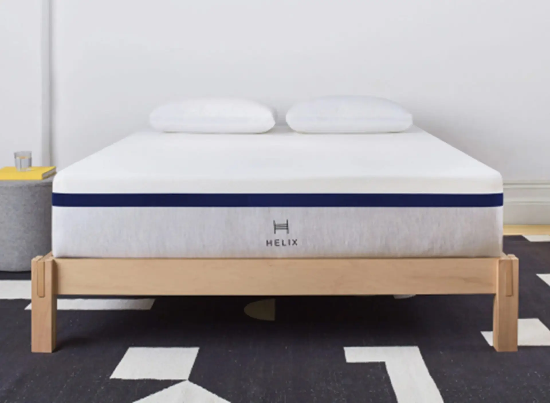 Helix Midnight 1 Helix Midnight mattress on a wooden bed frame with two white pillows, showcasing a medium feel design for comfort and pressure point relief.