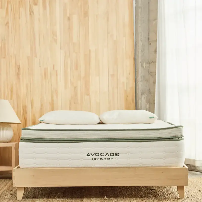 Avocado Green Mattress Box Top with plush pillows on a wooden platform bed, featuring a natural wood backdrop and soft lighting, emphasizing comfort and sustainability.