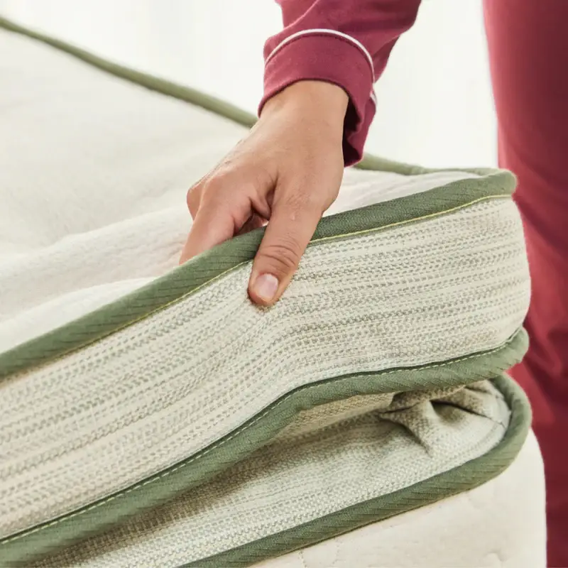 Hand gently holding the edge of the Avocado Green Mattress Box Top, showcasing its organic materials and plush design.