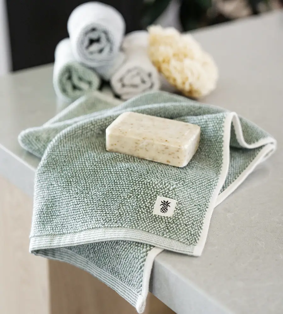 Cariloha Bamboo Two-Tone Washcloth 1 Cariloha Bamboo Two-Tone Washcloth on a countertop with a bar of soap and rolled towels, highlighting eco-friendly bath products.