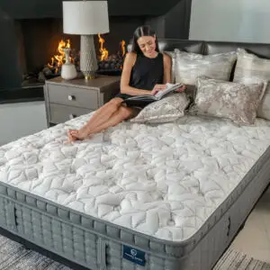 Woman reading on a King Koil mattress with plush bedding in a modern bedroom setting, showcasing comfort and luxury.