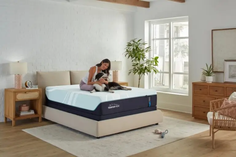Woman sitting on a Tempur-Pedic mattress in a bright bedroom, cuddling a dog, showcasing comfort and relaxation ideal for hot sleepers.
