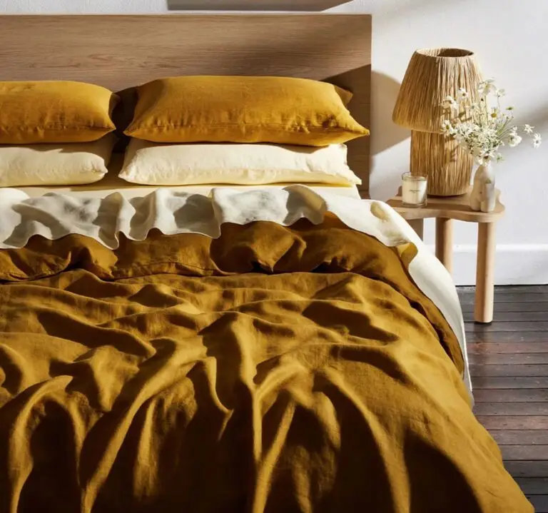 Stylish bedding arrangement featuring mustard and white linens, decorative pillows, and a wooden headboard, complemented by a bedside table with a lamp and flowers, ideal for autumn sleep comfort.