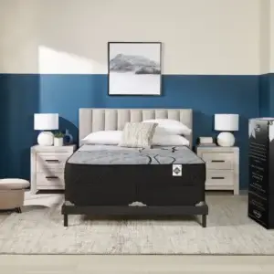 King Koil Cedar Firm Tight Top mattress displayed in a modern bedroom setting with blue accent wall, featuring bedside tables, lamps, and decorative wall art.