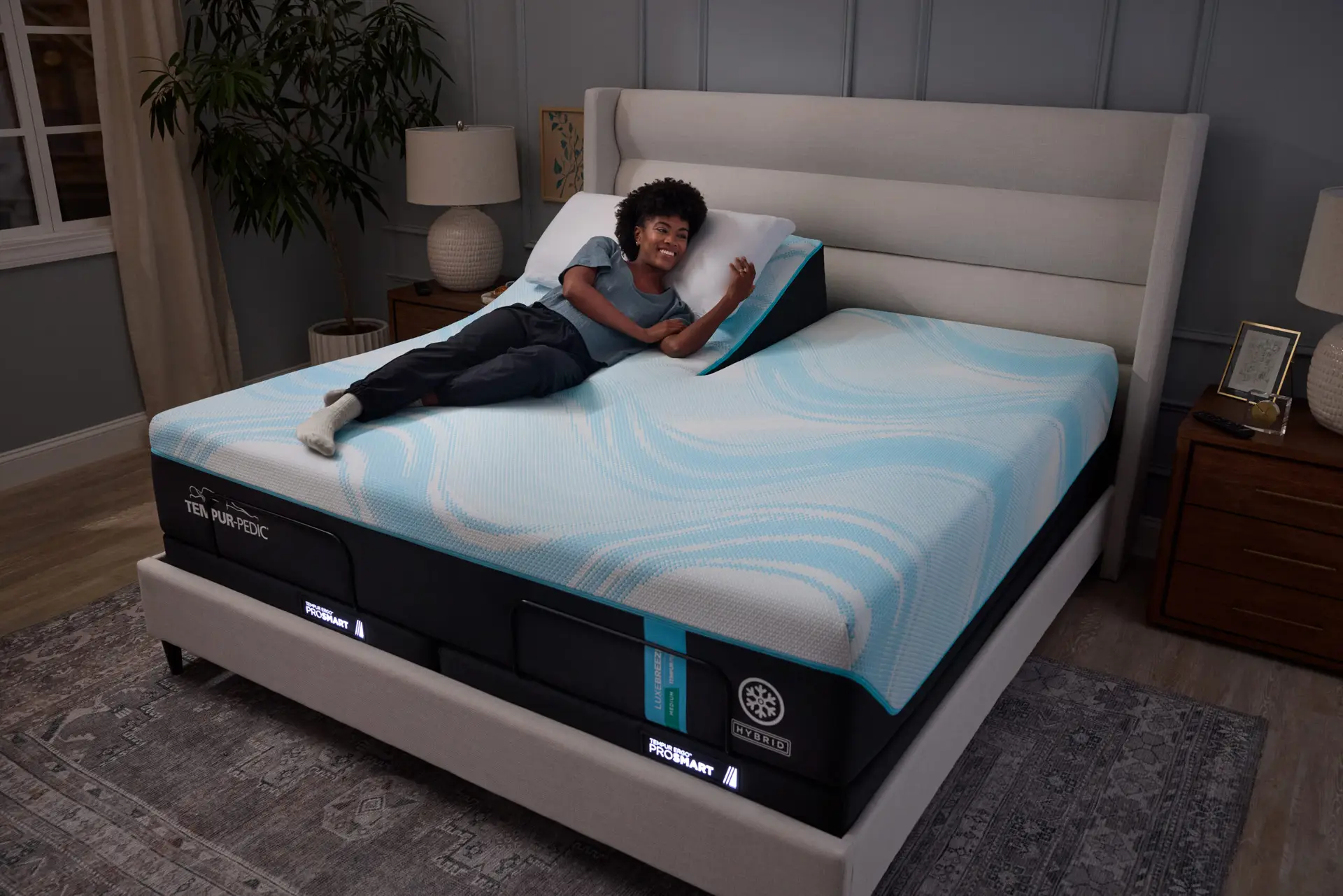 Woman relaxing on TEMPUR-Ergo® Power Base mattress, showcasing adjustable head and foot positioning, in a cozy bedroom setting with modern decor.