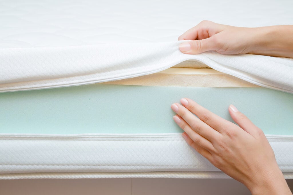 Complete Mattress Buying Guide for 2026: How to Choose the Best Bed for You 1 Hands inspecting a mattress cover revealing layers of foam, including memory foam, emphasizing mattress construction and material quality for informed sleep choices.